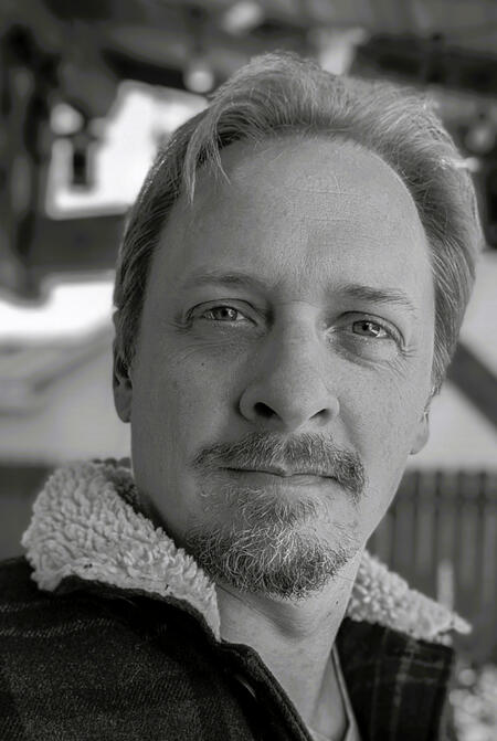 Christopher Brown - narrator B&W photo of a man with piercing eyes, a manly beard and hair that covers the entire top of his head no problem